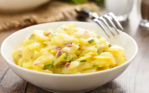 Schüssel mit cremigem Kartoffelsalat, garniert mit roten Zwiebeln und Schnittlauch. Ein köstliches Rezept für Kartoffelsalat!