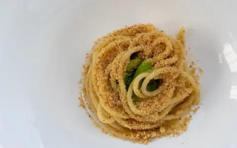 Spaghetti conditi con aglio, olio e peperoncino, cosparsi di pangrattato croccante e qualche foglia verde.
