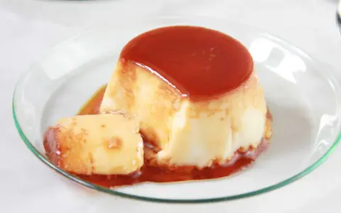 Delicioso flan de huevo en flanera con tapa, bañado en caramelo líquido y servido en un plato de cristal.