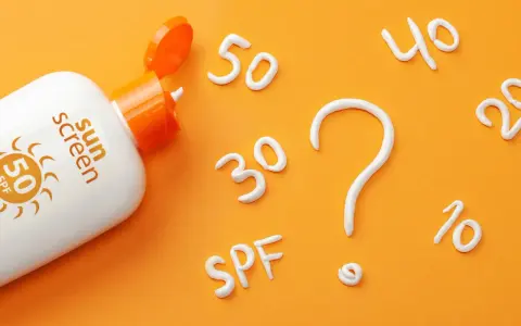Flacon de crème solaire SPF 50 ouvert, avec des chiffres (30, 40, 20, 10) et un point d'interrogation formés en crème. Quel indice choisir ?
