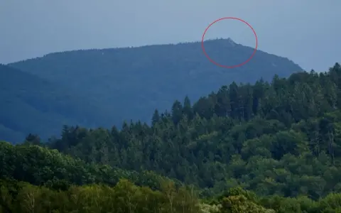 Górzyste krajobrazy czeskich Izery, z zalesionymi zboczami i skalistym szczytem zaznaczonym czerwoną obwódką.
