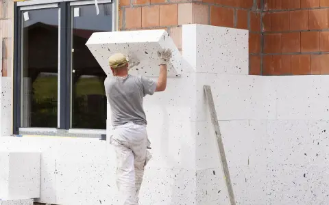 Budowlaniec montuje płyty ze styropianu grafitowego na elewacji. To dobry wybór, jaki styropian na elewację dla lepszej izolacji.