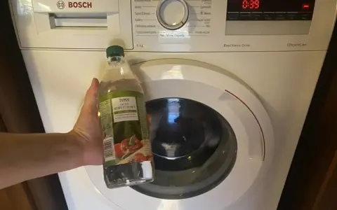 Ręka trzyma butelkę octu spirytusowego obok pralki Bosch. To początek domowego sposobu na mycie pralki octem.