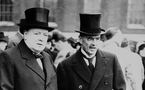 Winston Churchill und Neville Chamberlain, die die Appeasement-Politik kritisierten, tragen Zylinder.