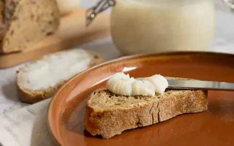 Ein Glas mit selbstgemachtem Schmalz steht bereit. Eine Scheibe Brot wird gerade mit dem Schmalz bestrichen, ein Genuss für jeden, der Schmalz selber machen möchte.
