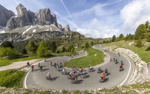 Ciclisti affrontano tornanti in una spettacolare salita alpe d'Huez, con maestose montagne sullo sfondo.