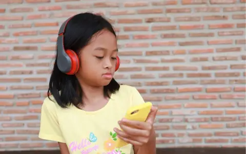 Dziewczynka w słuchawkach patrzy na telefon. Czy to przez to dzieci kłamią?
