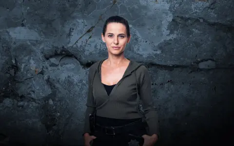 Natalia Brudniak w wojskowym stylu, z rękami w kieszeniach, na tle zniszczonej ściany.