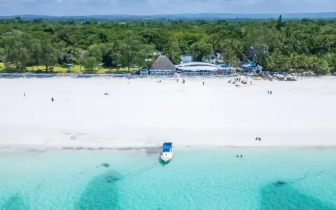 Idealne kenia wakacje: biała plaża, turkusowa woda, łódź i tropikalna roślinność.