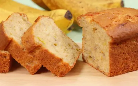 Fette di banana bread light, soffice e dorato, con banane mature sullo sfondo.