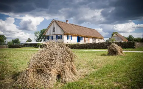 Tradycyjne chaty z krytymi strzechą dachami, jak te w skansenach w Polsce, otoczone plecionymi płotami i stogami siana.