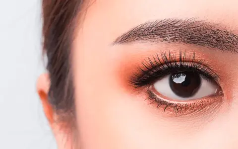 Occhi luminosi con un tocco di trucco coreano: ombretto pesca, eyeliner sottile e ciglia lunghe e folte.
