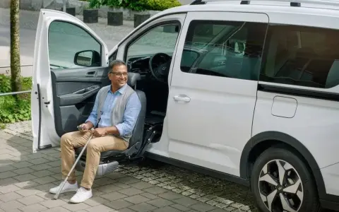 Hombre sonriente sentado en un asiento elevador de coche, listo para salir. Un ejemplo de soluciones de movilidad accesibles.