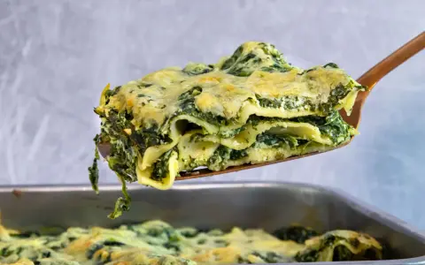 Ein Stück cremiger Ricotta Spinat Lasagne wird aus einer Auflaufform gehoben.