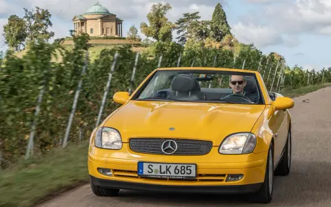 Gelber Mercedes SLK R170 Cabrio fährt durch Weinberge, im Hintergrund ein Tempel.