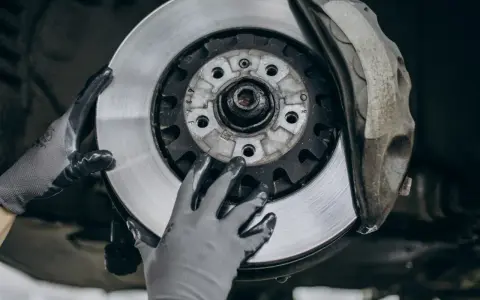 Mechanik w rękawiczkach wymienia zużyte tarcze hamulcowe. Widać nowy, lśniący element obok starego zacisku.