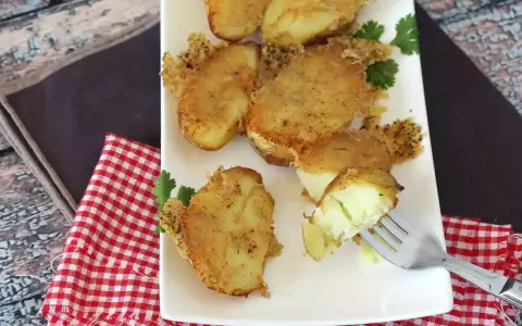 Krispiga, gyllene bitar av confiterad potatis, perfekt tillagade och serverade på en vit tallrik med en gaffel som visar den mjuka insidan.