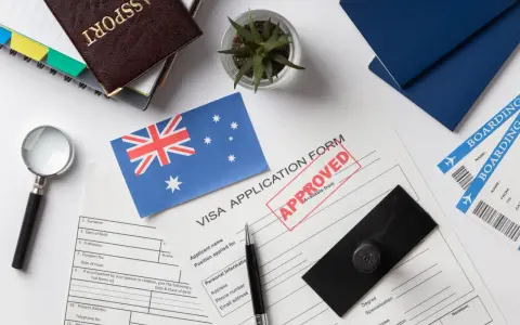 Paszport, formularz wizowy z pieczątką "APPROVED", flaga Australii, bilety lotnicze.