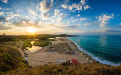 Zachód słońca nad bułgarską plażą w październiku. Spokojne morze, piaszczyste wydmy i zieleń.