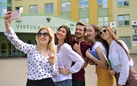 Studenci filologii angielskiej w Warszawie robią sobie selfie przed Uniwersytetem Vistula.