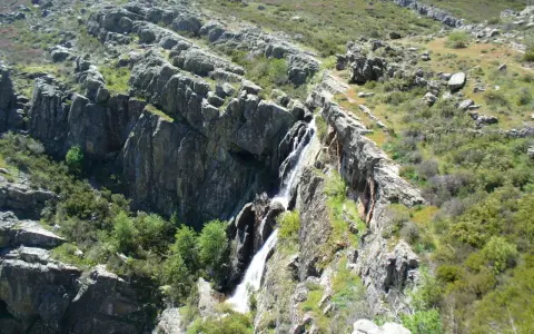 Cascada cayendo por rocas escarpadas cerca de un pico ocejon, rodeado de vegetación verde y rocas.