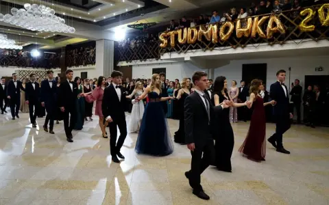 Młodzi ludzie w eleganckich strojach, tańczący poloneza na balu studniówkowym.