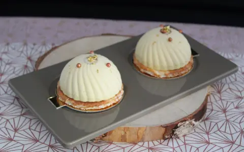 Deux dômes de dessert fruités, ornés de perles cuivrées et de feuilles d'or, reposent sur un plateau gris.