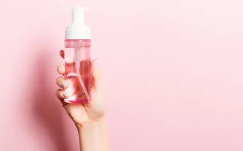Mano sostiene botella de agua micelar con dispensador. ¡Perfecto para cuando el agua micelar se enjuaga!