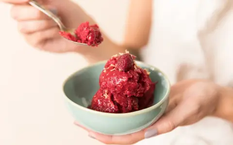 Ein Löffel Himbeersorbet-Rezept wird über eine Schüssel mit dem leuchtend roten Dessert gehalten, garniert mit einer Himbeere.