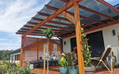 Drewniana pergola z przezroczystym dachem to idealne rozwiązanie co na dach tarasu. Wygodny wypoczynek wśród roślin i kwiatów.