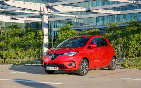 Czerwony Renault Zoe, elektryczny samochód miejski, gotowy do jazdy. Jego imponujący zasięg pozwala na swobodne podróżowanie po mieście i poza nim.