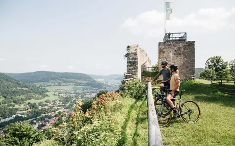 Zwei Radreisende genießen den Ausblick auf ein Tal mit einer Stadt und Ruinen. Perfekt für eine 5-tägige Radreise Deutschland.