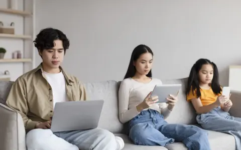 Trois personnes sur un canapé : un jeune homme sur un ordinateur portable, une femme sur une tablette, et une jeune fille sur un smartphone. Le temps d'écran recommandé pour 13 ans est dépassé pour certains.