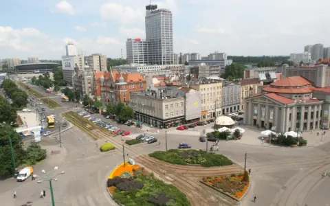 Widok na ruchliwy rynek w Katowicach z tramwajami, samochodami i budynkami.