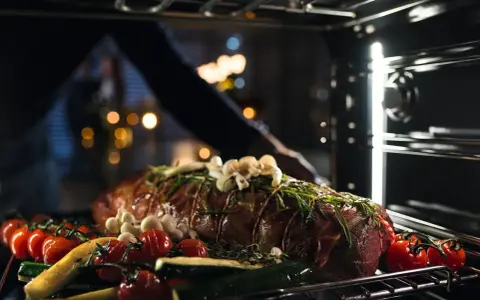 Ein Braten mit Kräutern, Knoblauch, Tomaten und Zucchini wird in den Ofen geschoben. So wird ein Dialoggarer zum Leben erweckt.