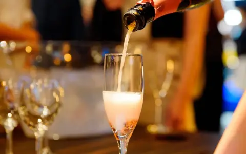Nalewanie musującego **cava wino** do kieliszka. W tle widać inne kieliszki i rozmyte światła, sugerujące uroczystą atmosferę.
