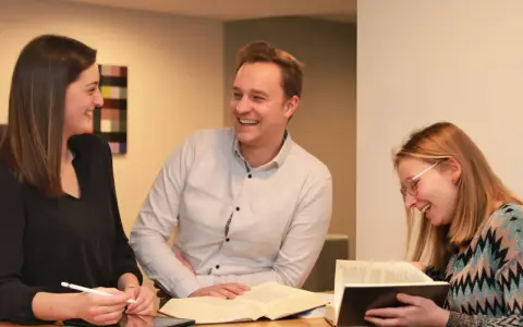 Drei Personen lernen gemeinsam. Sie diskutieren und lachen, vielleicht über den Weg, wie wird man Pastor.