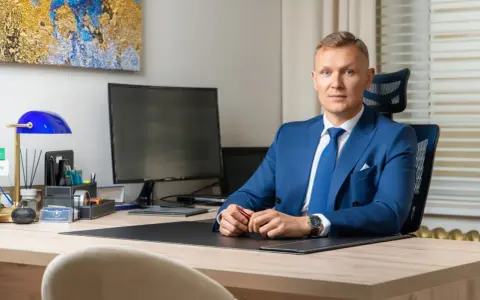 Mężczyzna w niebieskim garniturze siedzi przy biurku w nowoczesnym biurze.