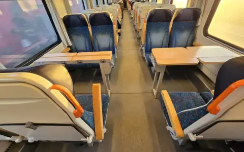 Pociąg do Pragi. Puste siedzenia z niebieskimi obiciami i stolikami czekają na pasażerów.