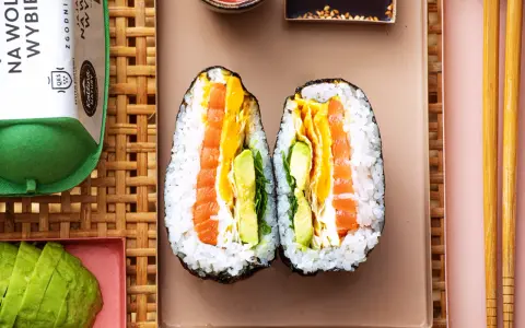 Dwa połówki onigiri z łososiem, awokado i jajkiem, podane na talerzu z pałeczkami.