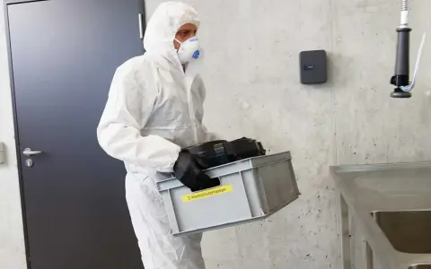 Hombre con traje blanco y mascarilla, lleva caja con equipo de protección obligatoria de vías respiratorias.