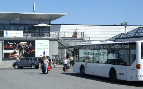 Autobus wahadłowy na lotnisko Oslo Torp. Ludzie z bagażami wychodzą z terminala.