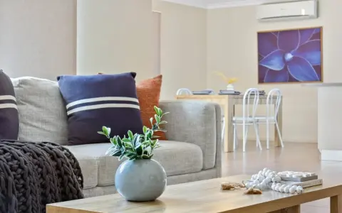 Soggiorno moderno con divano grigio, cuscini decorativi e un condizionatore per rendere smart l'ambiente. Tavolo da pranzo e quadro floreale sullo sfondo.