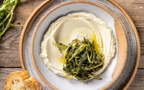 Crema di fave e cicoria saltata, servita su un piatto rustico con pane croccante.