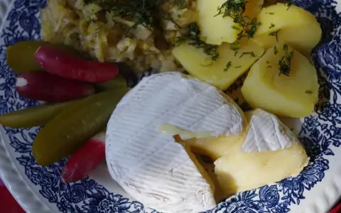 Częściowo roztopiony camembert z ziemniakami, ogórkami kiszonymi i rzodkiewką na talerzu.