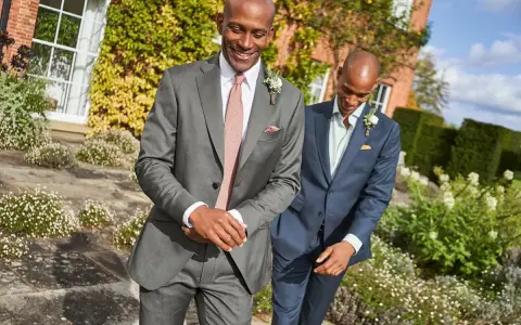 Two men in suits walk outdoors. The question "do you have to wear a suit to a wedding?" is answered by their stylish attire.