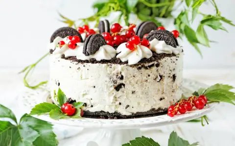 Pyszny tort z kawałkami oreo ciastka, udekorowany bitą śmietaną i czerwonymi porzeczkami.
