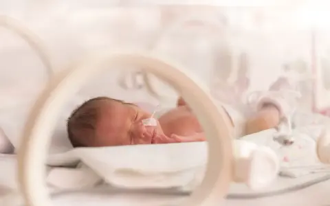 Maleńki wczesniak w inkubatorze, z rurką w nosku, śpi spokojnie.
