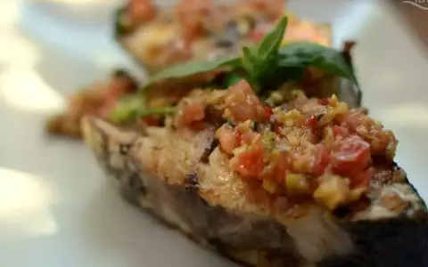 Deliciosa corvina a la plancha con un sofrito de tomate y hierbas frescas, servida en un plato blanco.