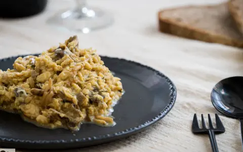 Delicioso revuelto de setas servido en plato oscuro, acompañado de pan y cubiertos.